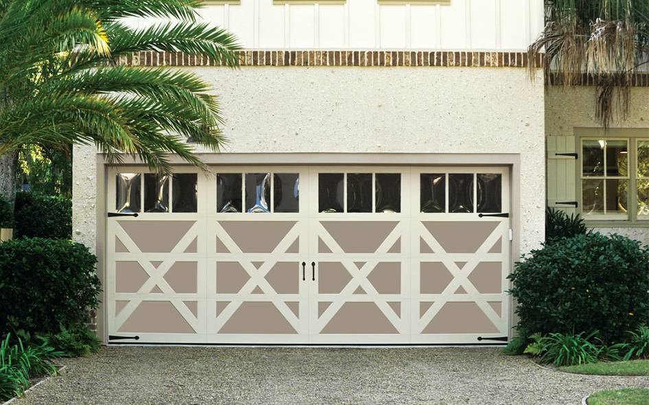 A cream and beige garage door with a decorative crisscross pattern and small rectangular windows at the top, set in a stucco house with plants and a palm tree nearby.