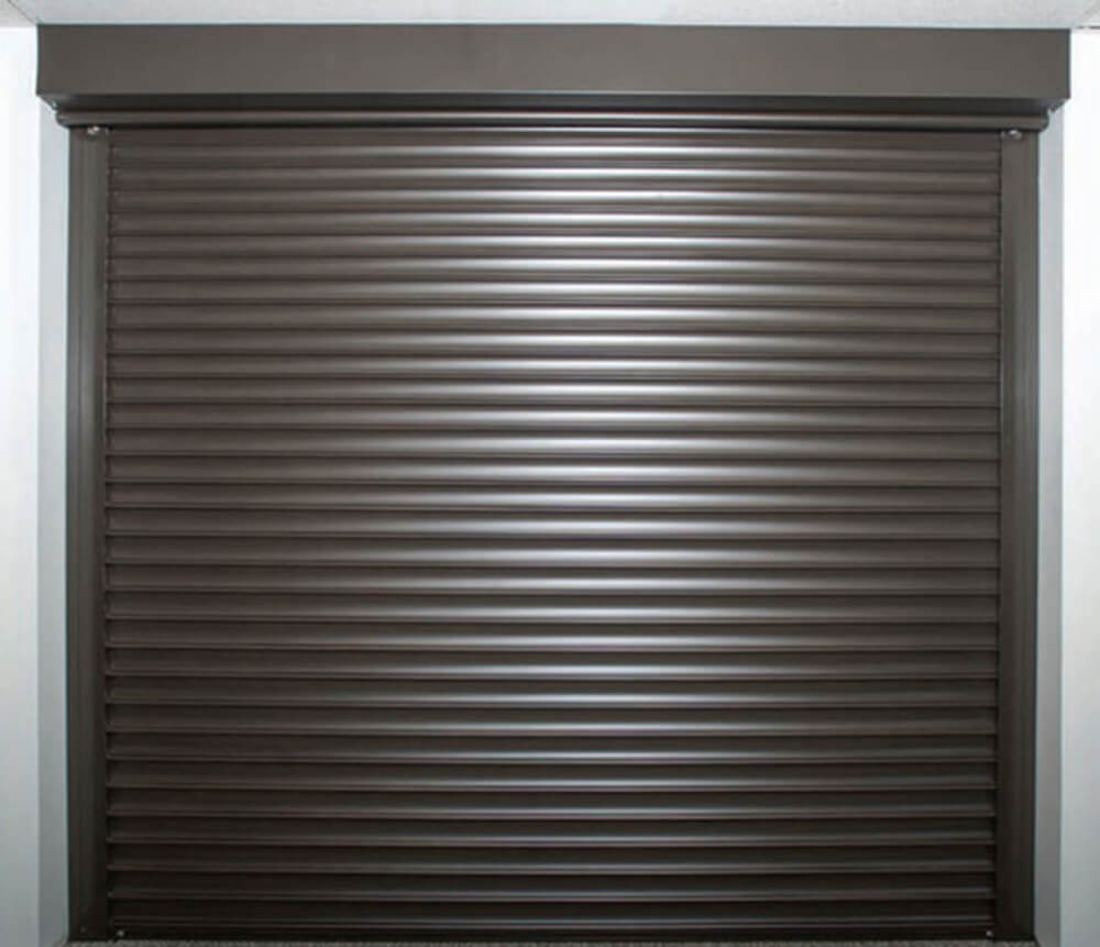 A closed brown metal roller shutter door, fitted within a rectangular frame, with horizontal slats visible across its surface.
