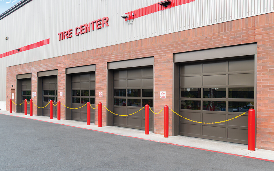 A brick building labeled Tire Center with four closed garage doors, red posts connected by yellow chains, and a paved driveway in front.