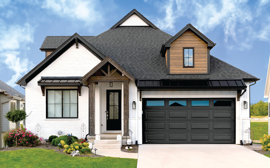 Modern suburban house with white brick exterior, black roof and trim, a wooden accent above the garage, large steel garage doors in black, landscaped front yard, and clear blue sky in the background.