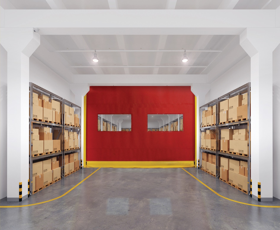 A warehouse interior with shelves of cardboard boxes on both sides, a polished concrete floor, and a bright red wall featuring a High Speed Door and two rectangular windows at the far end. Yellow lines mark pathways on the floor.