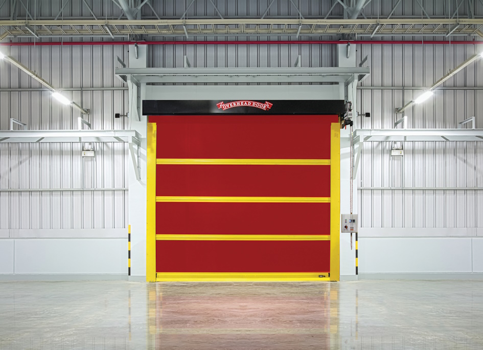 A large, bright red high speed door with yellow borders is installed in a clean, modern warehouse with metallic walls and a polished concrete floor.