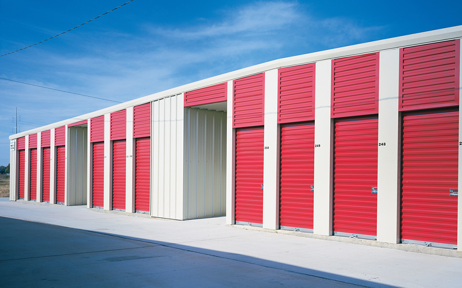 A row of storage units with Model 770SS rolling sheet doors and white trim on a sunny day, set against a clear blue sky and paved ground.