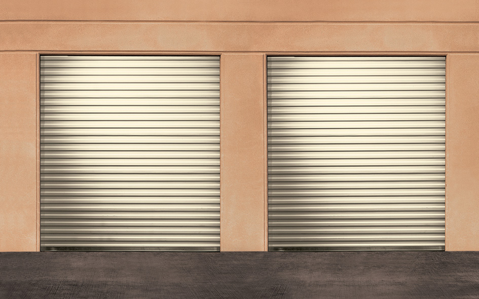 Two closed Model 780CD rolling sheet doors set in a beige wall, with a concrete ground in front.