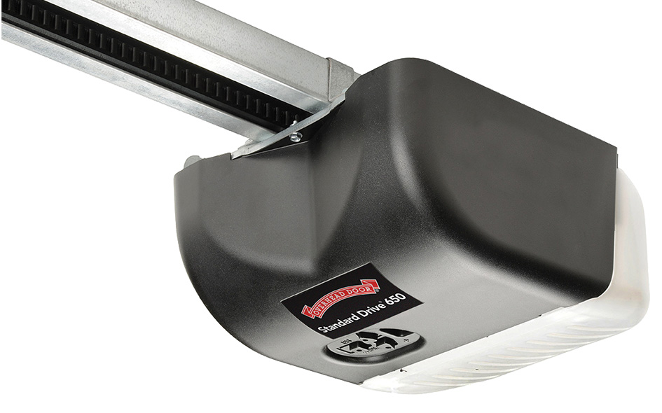 A close-up view of a black Legacy 650 garage door opener labeled Standard Drive 850, mounted on a metal rail, with a white light cover on one end.