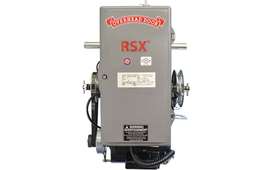 Gray industrial RSX fire door operator with “Overhead Door” logo at the top, control labels, warning stickers, and visible gears and wiring on the sides. Ideal for fire door automation. Photographed against a white background.